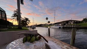 A waterfront scene with a mosaic-tiled bench, palm trees, and a calm water body. - A beautiful spot to unwind, relax and enjoy quality time with family and friends (Cape Coral)