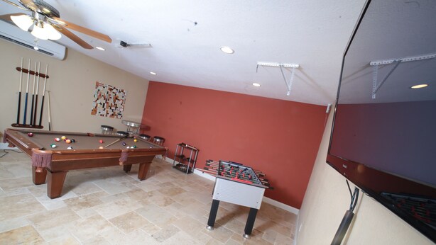 A pool table, foosball table, and billiards equipment in a room with red walls and tiled flooring.