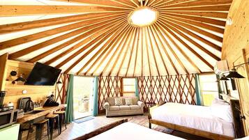 L’intérieur d’une yourte, avec une coupole centrale, un canapé, un lit, un bureau avec un ordinateur et un coin cuisine.