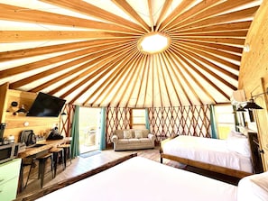 A yurt interior with a central dome, a sofa, a bed, a desk with a computer, and a kitchen area. - Glamping Yurt near Zion with Sunset Views (Orderville)
