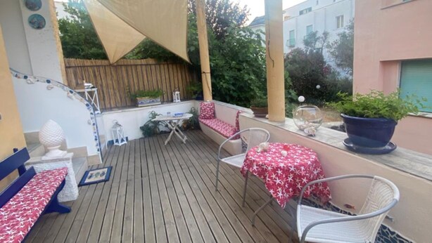 Een houten terras met een tafel, stoelen, een bank en een beschaduwd gedeelte met een zonnescherm.