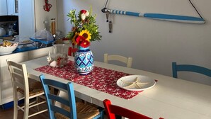 A dining area with a white table, blue and red chairs, a vase with flowers, and a ceiling light fixture made of driftwood. - Rosanna Maison B&B (Ischia)