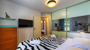 Una habitación de hotel moderna con una cama a rayas de cebra, un aparador de madera, un televisor de pantalla plana y un espejo grande que refleja la habitación.