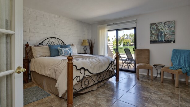 A bedroom with a bed, a chair, a small table, and a painting on the wall.
