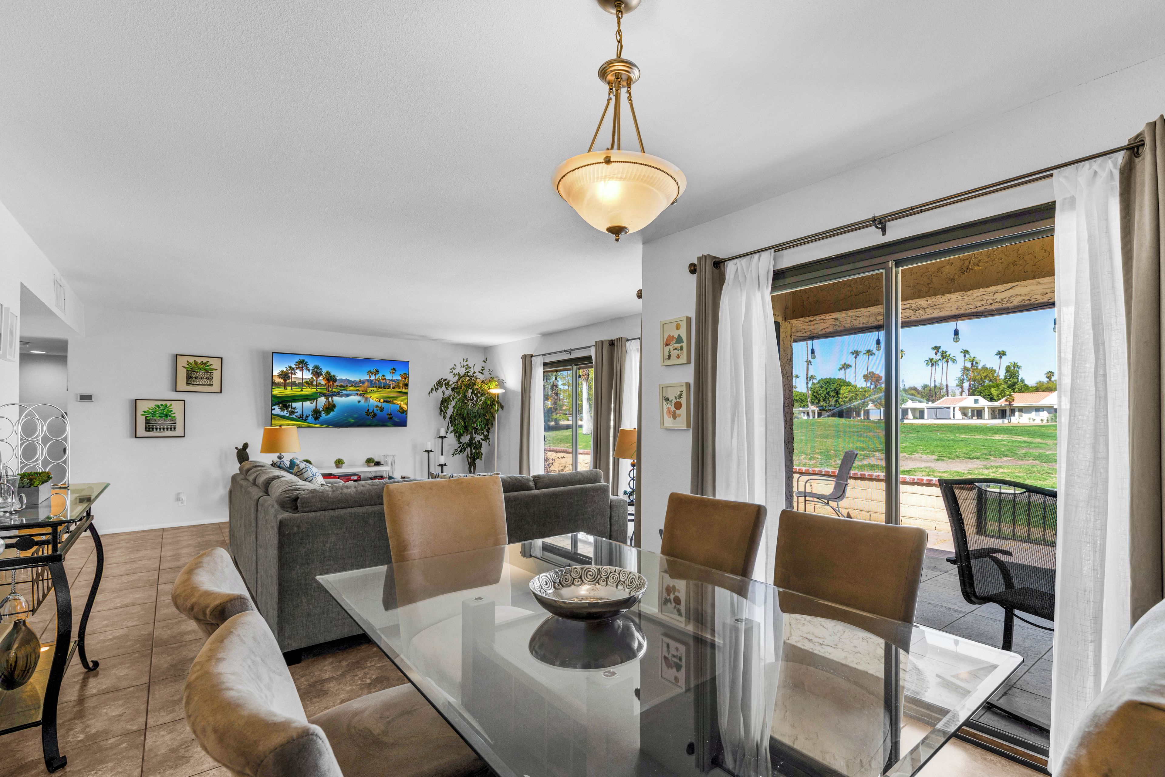 A modern living room with a glass dining table, grey sofa, and a view of a golf course through large windows.