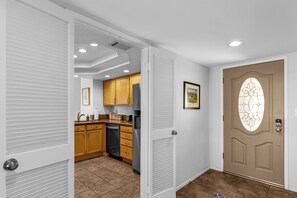 A hallway leading to a kitchen with wooden cabinets, a refrigerator, and a door with a decorative glass window.