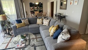 A living room with a grey sectional sofa, a glass coffee table, and a patterned rug.