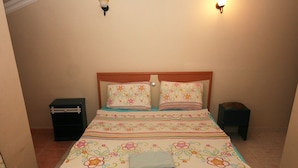 A bedroom with a bed, pillows, a nightstand, and a wall-mounted light fixture.
