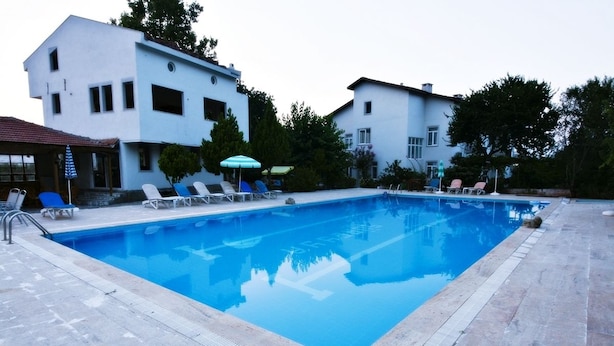 A swimming pool with lounge chairs and umbrellas, surrounded by buildings and trees.