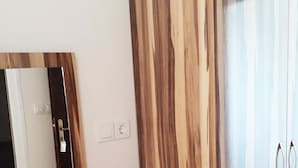 A room with a wooden vanity, a mirror, a white wall, and a wardrobe with a striped curtain.