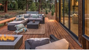 A wooden deck with outdoor furniture, a fire pit, and a glass-enclosed area with a stone fireplace. - Mountain Modern Home in the Signature Collection at Old Greenwood! (Truckee)