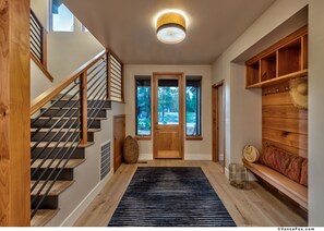 Un interior moderno con una escalera de madera, un tapete a rayas blanco y negro, y un banco de madera con una cesta tejida.