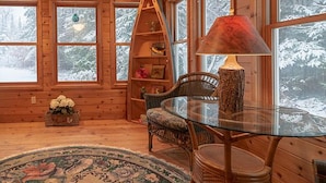 A cozy cabin interior with a glass table, wooden walls, and a large window offering a snowy forest view. - Walk To The Lake, Beach, Indoor Waterpark And Downtown (Mackinaw City)