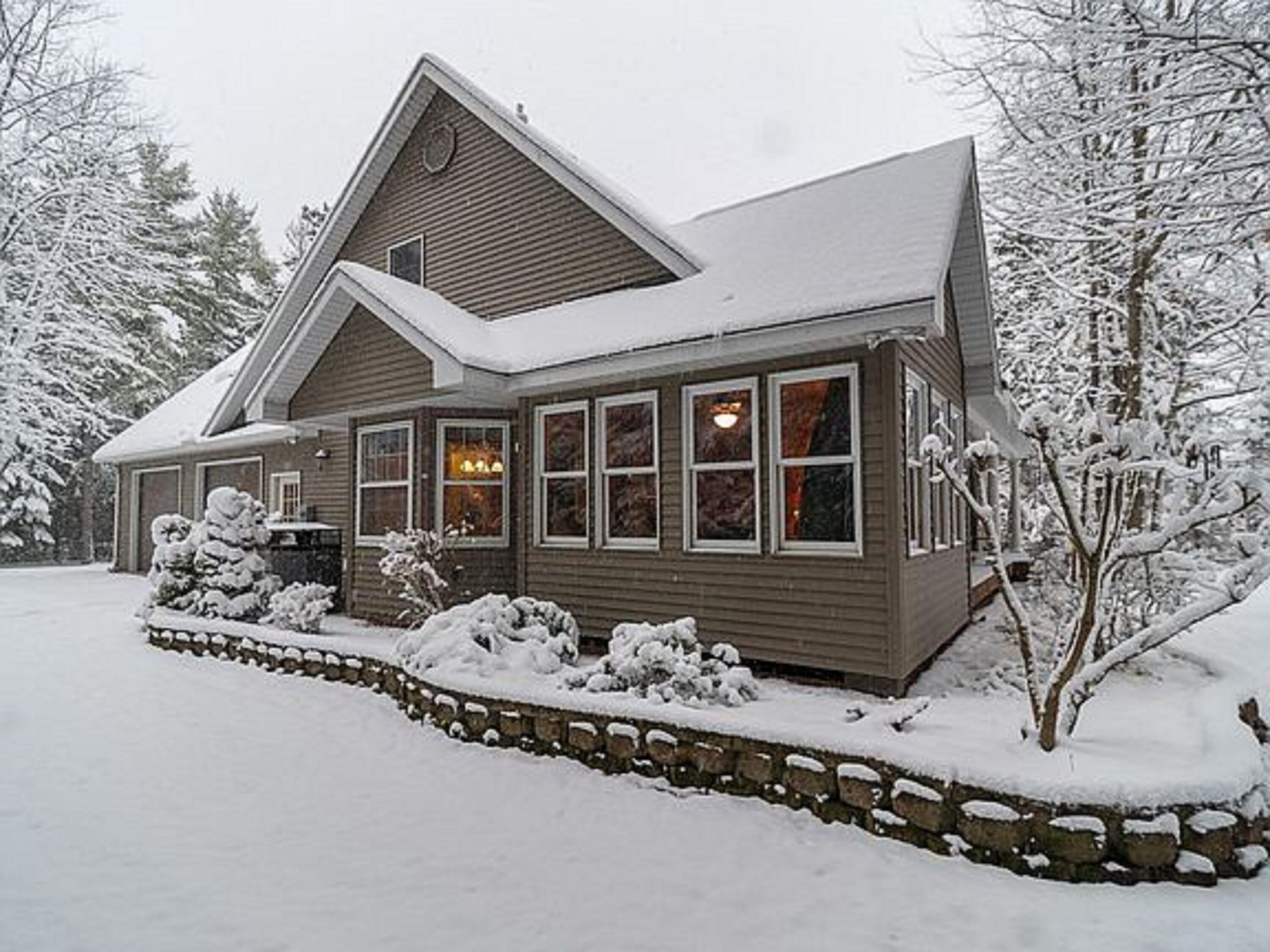 Une maison à deux étages, avec des fondations en pierre et un toit recouvert de neige.