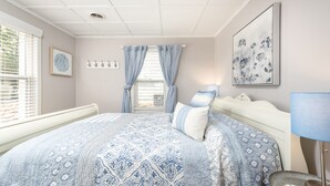 Ein Schlafzimmer mit einem großen Bett, einem Fenster mit Jalousien, einem Wandbild und einem Nachttisch mit Lampe.