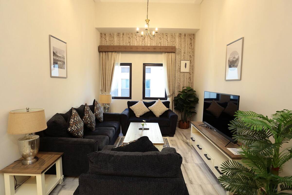 A modern living room with a sofa set, a coffee table, a TV, and a chandelier.
