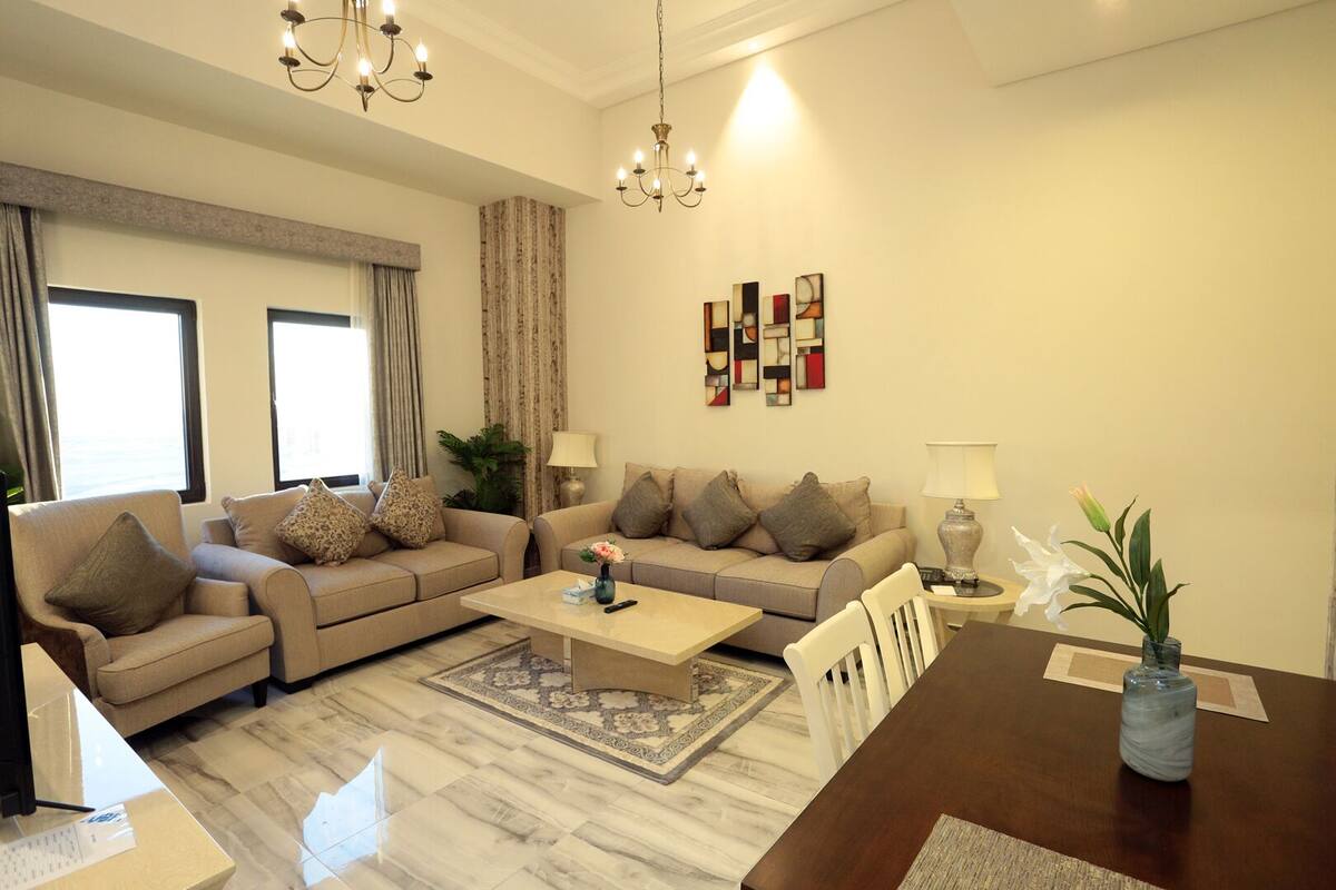 A living room with a sofa set, a coffee table, a dining table, and a chandelier.