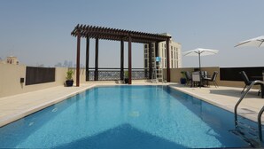 A rooftop swimming pool with a pergola, outdoor seating, and a view of the city skyline. - Marbella Holiday Homes (Dubai)