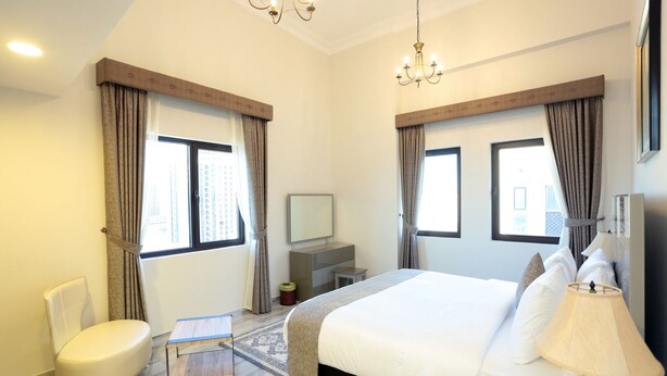 A modern hotel room with a large bed, a desk, a chair, and a TV. - Marbella Holiday Homes (Dubai)