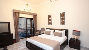 A spacious bedroom with a large bed, two bedside tables with lamps, a TV, a balcony with curtains, and two decorative wall pieces. - Marbella Holiday Homes (Dubai)