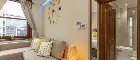 A modern living room with a sofa, decorative pillows, a wall clock, and a lamp.