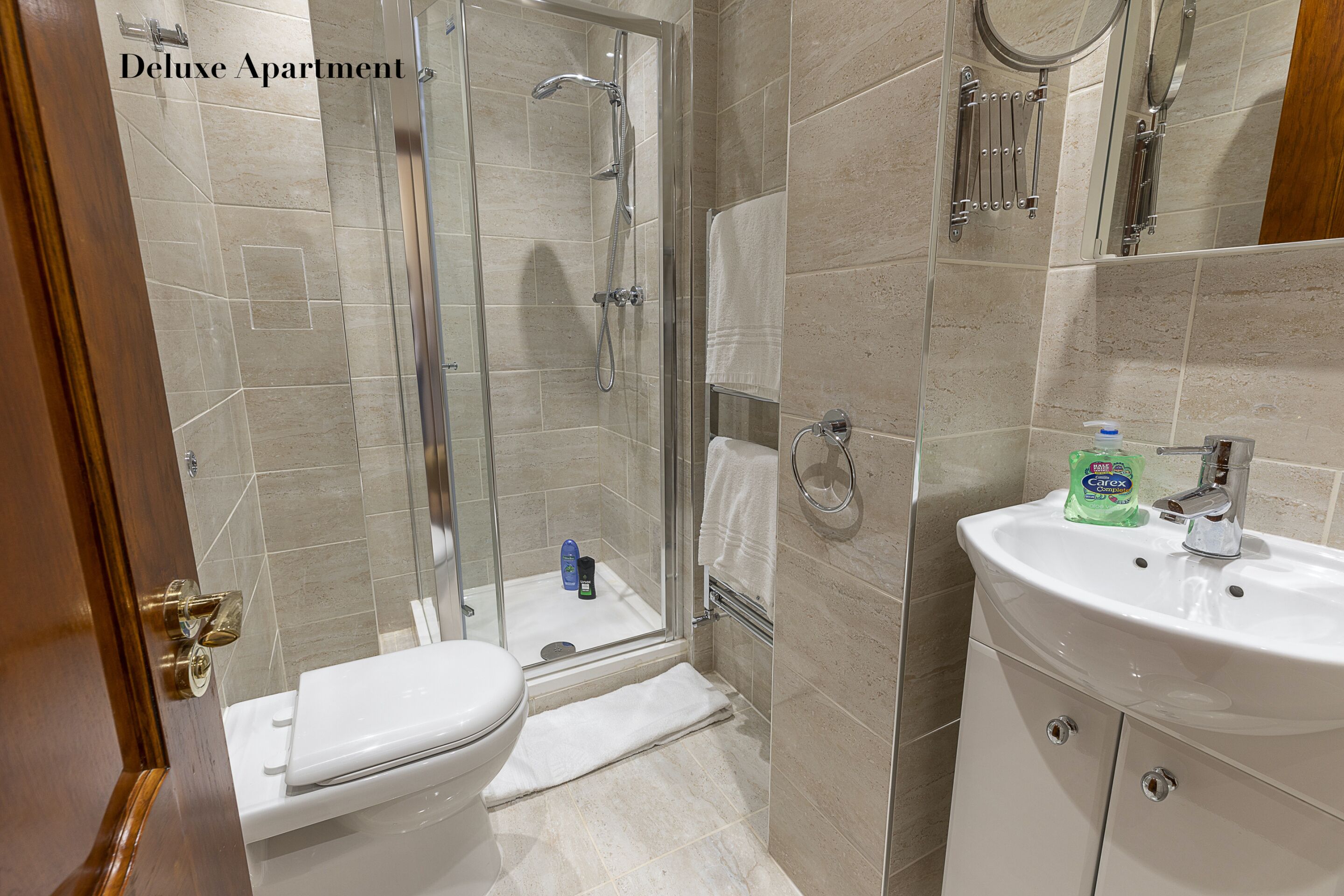 A bathroom with a toilet, a glass-enclosed shower, and a sink with a bottle of Carex soap.