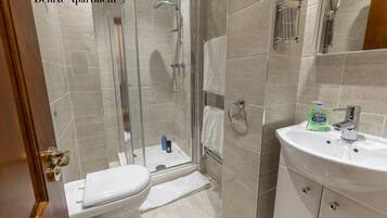 A bathroom with a toilet, a glass-enclosed shower, and a sink with a bottle of Carex soap.