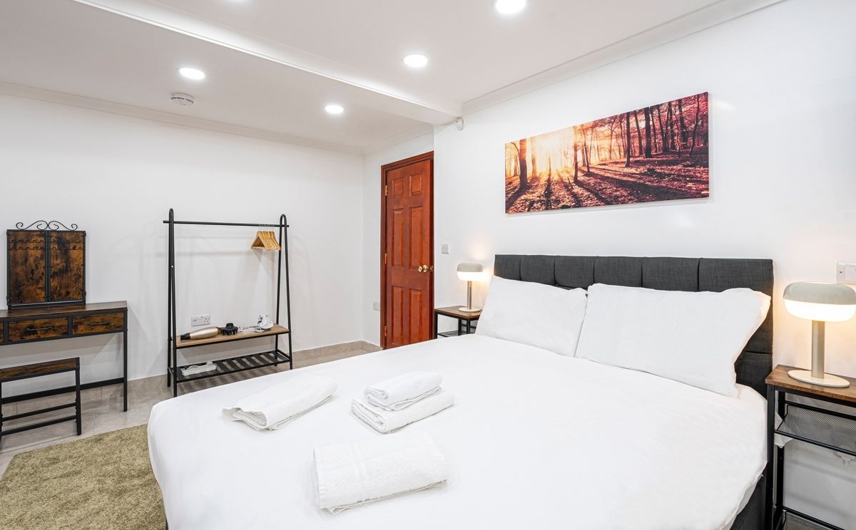 A hotel room with a bed, bedside tables, a wardrobe, a mirror, and a painting on the wall.