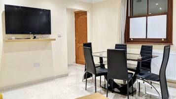 A conference room with a flat-screen TV, a wooden door, a window with blinds, and a table with chairs.