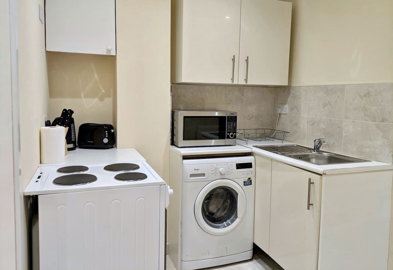 A compact kitchen with a stove, microwave, washing machine, and sink.