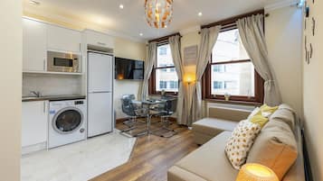 A compact living space with a kitchenette, a sofa, a dining table, and a TV.