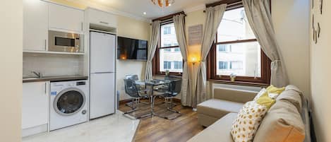 A compact living space with a kitchenette, a sofa, a dining table, and a TV.