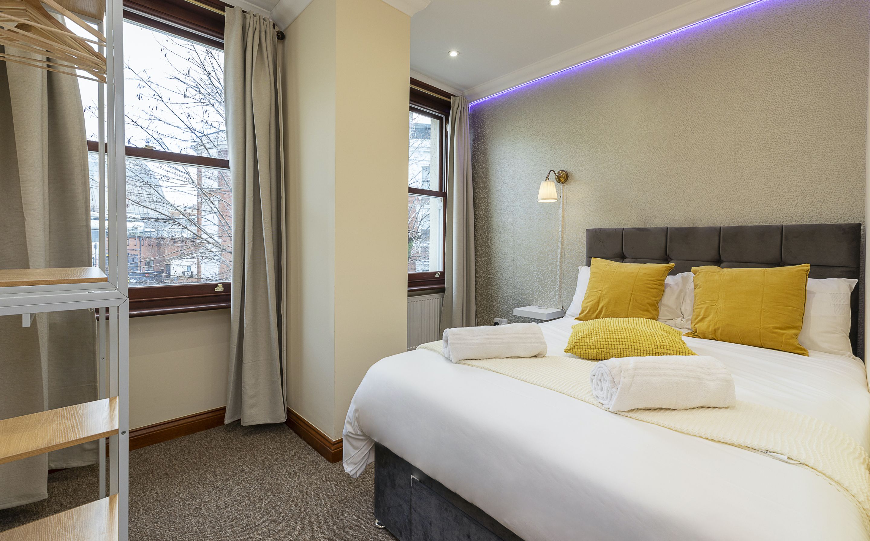 A hotel room with a bed, a bedside table, a lamp, and a window with curtains.