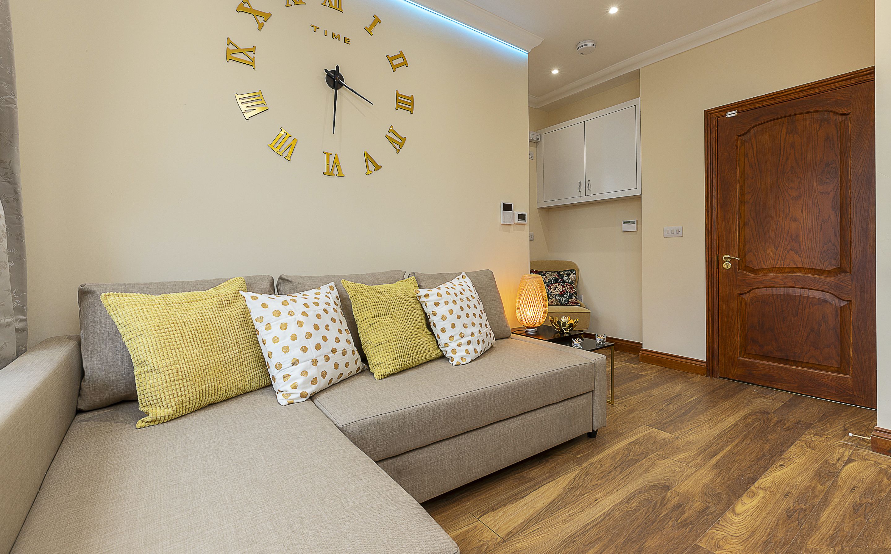 A living room with a sofa, a wall clock, a wooden door, and a cabinet.