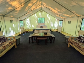 Alojamento em tenda com uma cama central, uma mesa e dois sofás.