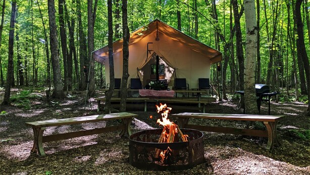 Un terrain de camping aménagé dans une forêt, avec une tente, un foyer et des tables de pique-nique.