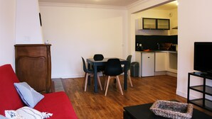 A living room with a red sofa, a dining table with chairs, a TV on a stand, and a kitchen in the background. - 2 rooms in the heart of Granville, Saint-Paul district (Granville)