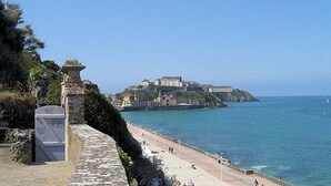 A coastal view with a stone wall, a beach, and a castle on a hill. - 2 rooms in the heart of Granville, Saint-Paul district (Granville)