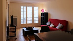 A living room with a red sofa, a black cabinet, a wooden coffee table, and a black TV stand. - 2 rooms in the heart of Granville, Saint-Paul district (Granville)