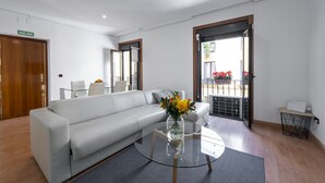 A modern living room with a white sofa, a glass coffee table with a vase of flowers, and a door marked "SALIDA". - Madrid Centric IV (Madrid)