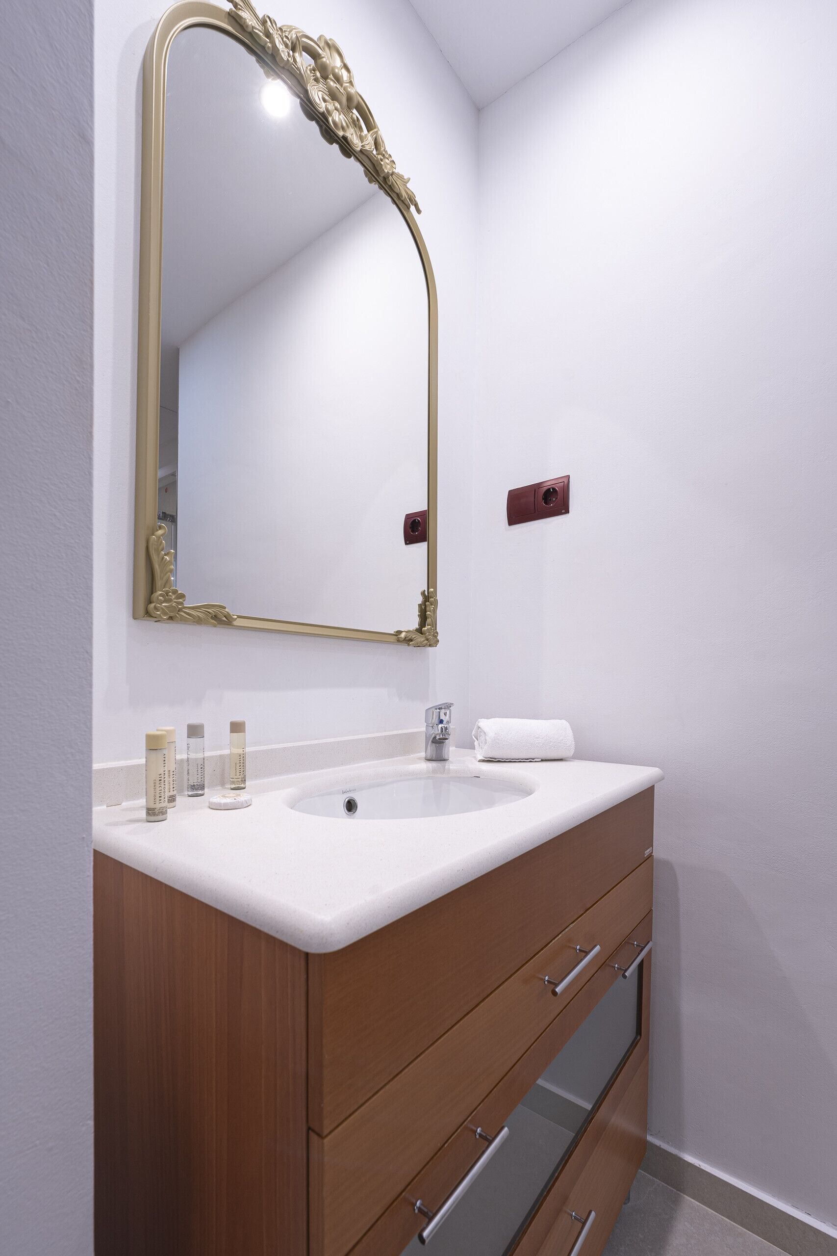 A bathroom with a white vanity, a gold-framed mirror, and a wooden cabinet with drawers.