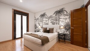 A bedroom with a bed, a nightstand, a door, and a wall with a tropical mural. - Madrid Centric IV (Madrid)
