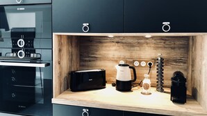 Moderni keittiö, jossa on mustat kaapit, puinen työtaso, Bosch-merkkinen mikroaaltouuni, Philips-merkkinen kahvinkeitin ja sokeriastia.