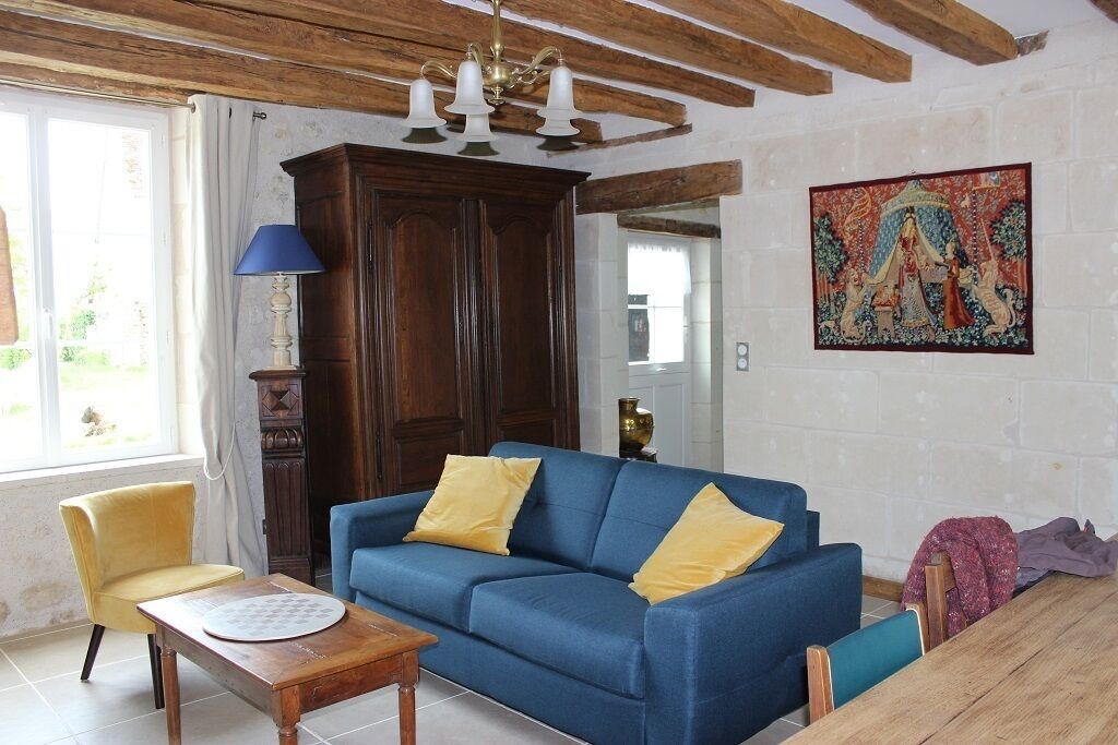 Een woonkamer met een blauwe bank, gele kussens, een houten tafel, een gele fauteuil, een blauwe lamp, een houten kast en een kleurrijk wandtapijt.