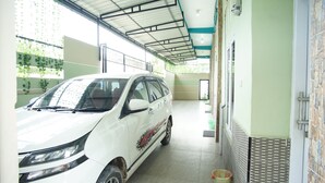 A white minivan parked in a covered parking area with a tiled floor and a green wall with a patterned design. - Wisma Pandowo (Inderapura)