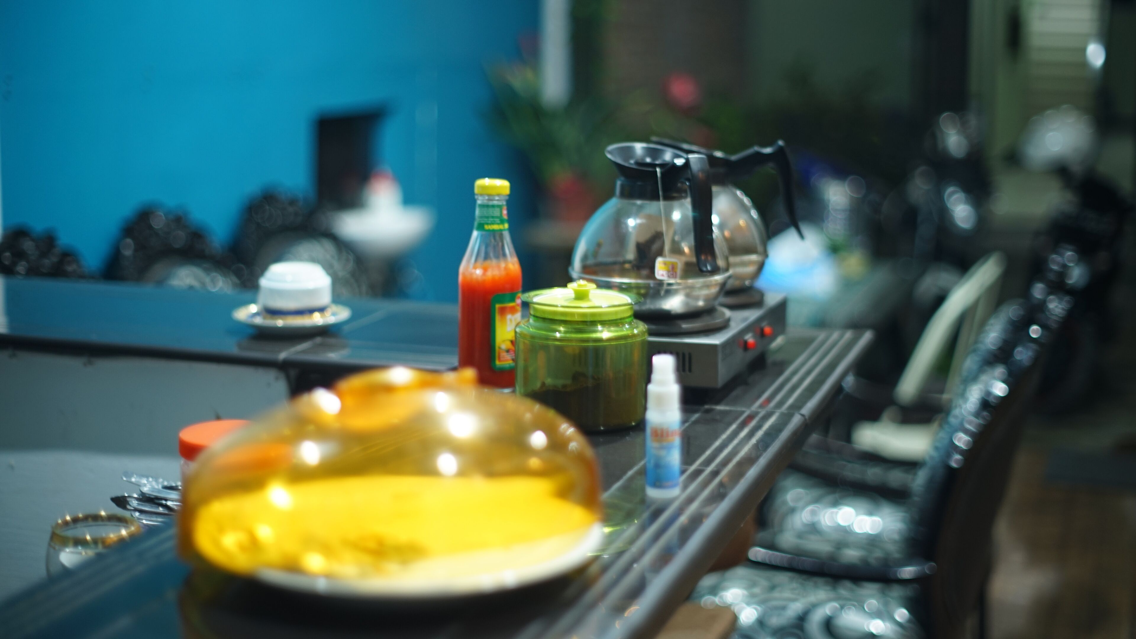 Una mesa de comedor con diferentes condimentos, un frasco de vidrio y una cafetera.