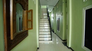 A long, narrow hallway with a staircase leading to an upper floor. The walls are painted a light green, and there are several doors and windows along the hallway. - Wisma Pandowo (Inderapura)
