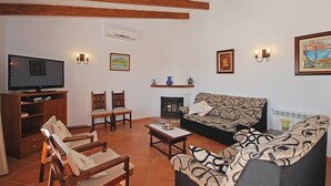 Una sala de estar con televisor, sillas de madera, sofá, chimenea e iluminación en la pared.