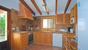 Una cocina con armarios de madera, horno empotrado, lavavajillas y ventana con vistas al exterior.