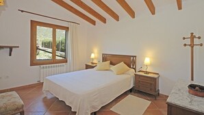 Un dormitorio con cama, lámparas de noche, ventana con vistas, radiador y techo de madera.